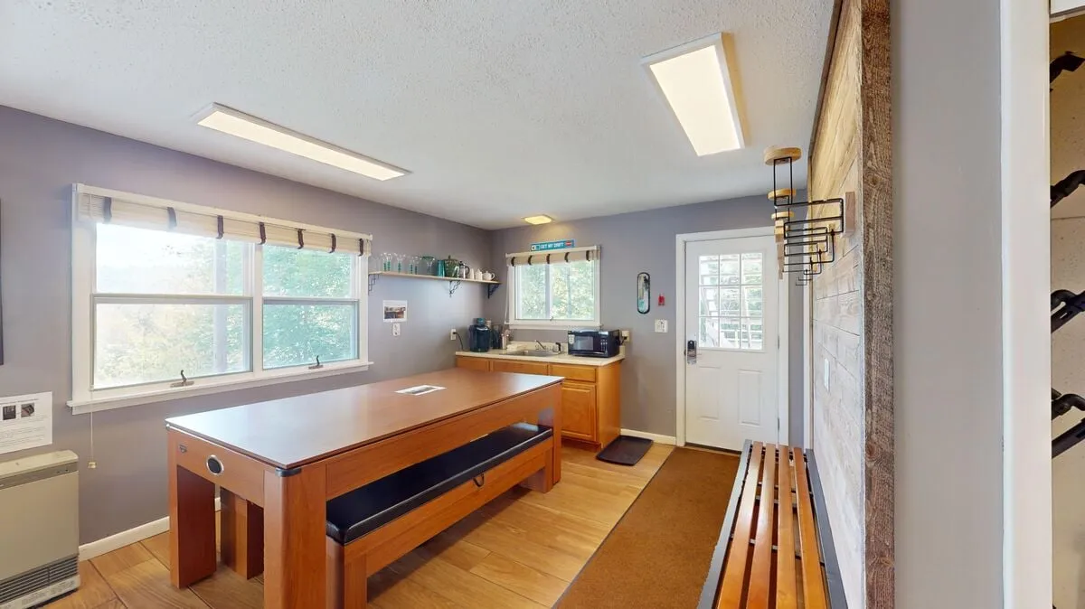 This image depicts a large wooden table set in a cozy kitchenette area, with a door leading outside and a window offering scenic views. The space feels inviting and is ideal for casual dining, family gatherings, and socializing.