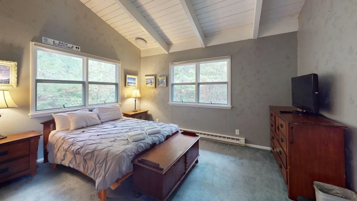A serene bedroom with a large bed, window, dresser, and TV. The room is filled with natural light, creating a calm and restful atmosphere ideal for privacy and relaxation.