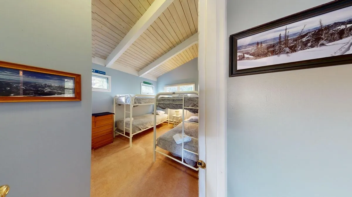 A cozy bunk bed room featuring wooden beams, framed pictures, and windows that let in morning light. The arrangement invites both restful nights and casual, late-night chats.