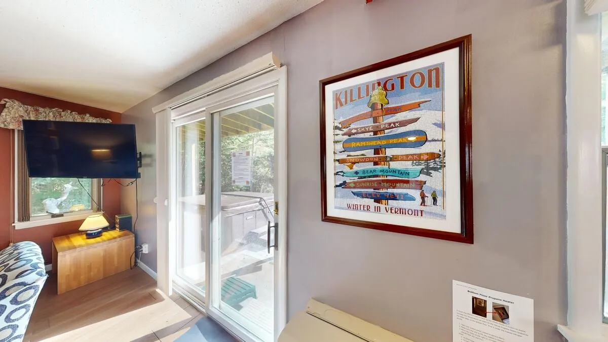 Inside, a comfortable seating area features colorful artwork and a sliding glass door, blending local culture with access to the outdoors. Natural light fills the space, and the visible television and decor offer a taste of the chalet’s inviting ambiance.