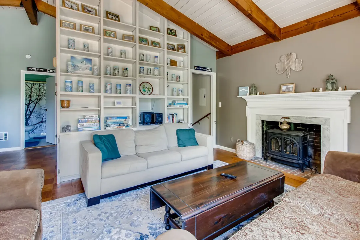 A warm living area with a comfortable sofa, tall bookshelf, fireplace, and coffee table. The space is ideal for reading, socializing, and relaxing by the fire.