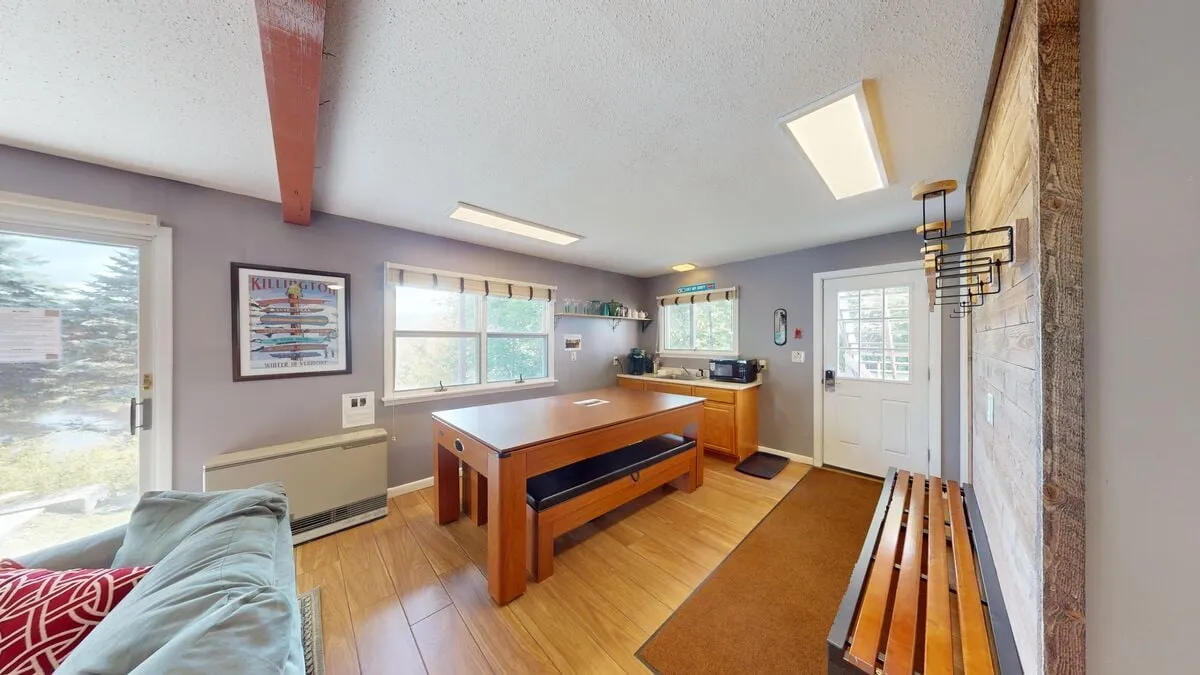A spacious dining area featuring a large wooden table surrounded by comfortable seating, with windows letting in plenty of natural light. A cozy adjoining seating area and wooden bench create an inviting spot for shared meals and group gatherings.