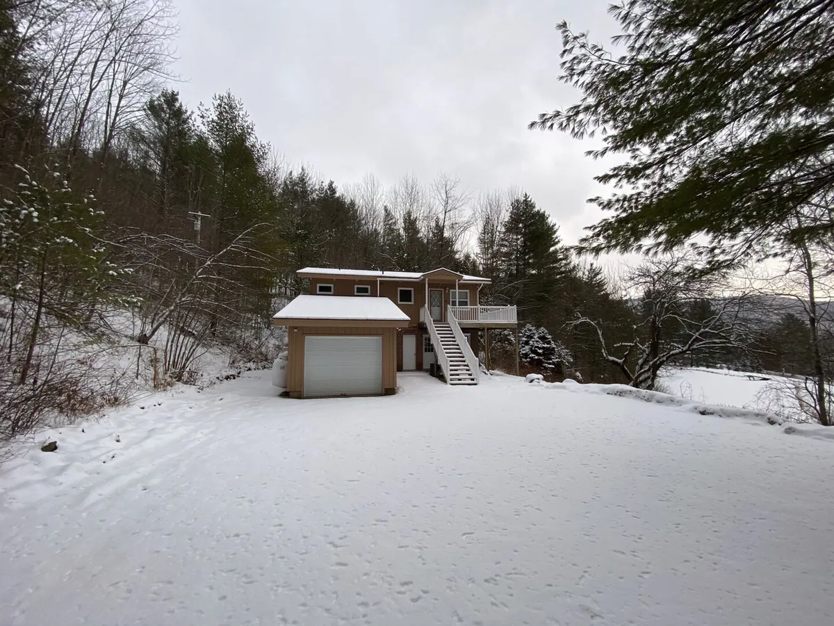 A snow-covered chalet nestled among tall trees, with the house as the central focus. The peaceful landscape is blanketed in fresh snow, suggesting proximity to winter activities and offering a sense of seclusion ideal for après-ski relaxation. A fire pit in the yard hints at gathering spots for guests after outdoor adventures.