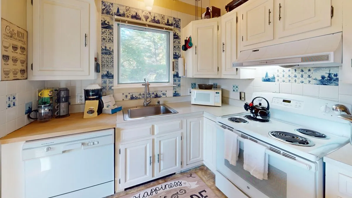 A warm, fully equipped kitchen with a view through the kitchen window, a stove, sink, decorative tiles, and a cozy rug. The setup invites culinary adventures, from cooking family recipes to casual breakfasts and festive feasts.