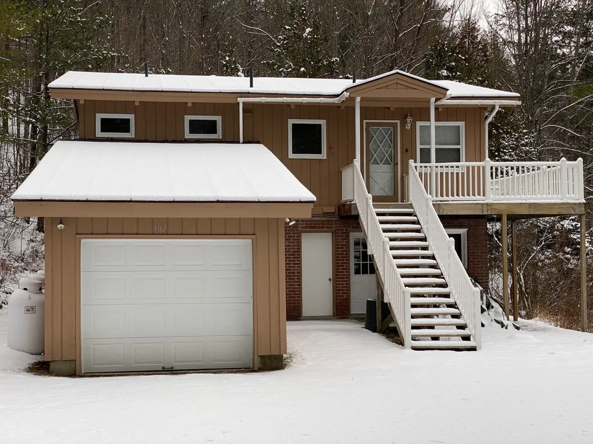 The image captures the chalet's front entrance, staircase, garage door, and deck, with wintry elements visible that hint at the home’s inviting approach and connection to the outdoors. The deck and surrounding space suggest a place to enjoy changing seasons and stunning views.