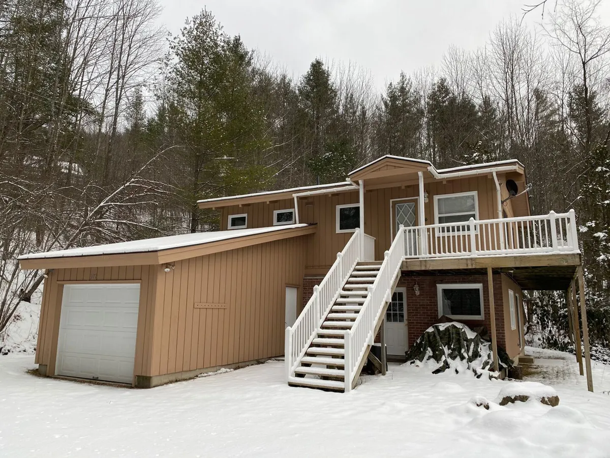 This image captures the exterior of the property, highlighting a staircase leading to the entrance, a garage, and a balcony area dusted with snow. The inviting front, visible yard, and outdoor features establish a strong sense of arrival and set the context for local exploration.