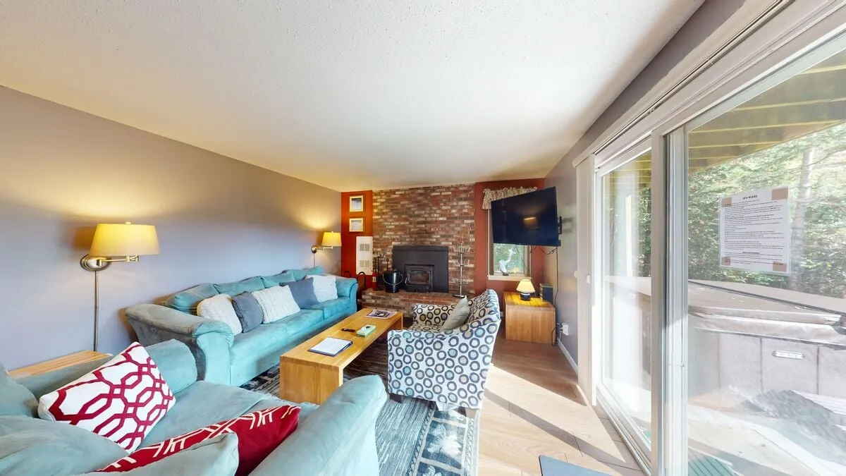 A cozy interior living area with a sofa seating arrangement, fireplace, television, and a prominent window revealing an outdoor view. The space invites relaxation after a day spent outside.