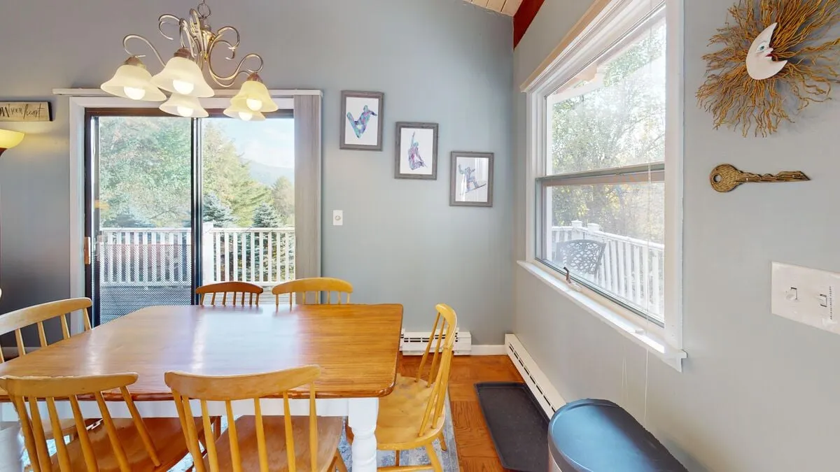 A warm and welcoming dining area featuring a central table under a stylish chandelier, framed by sliding glass doors and tasteful artwork. The setup exudes a homey, functional vibe suitable for group dining, games, or collaborative work sessions.