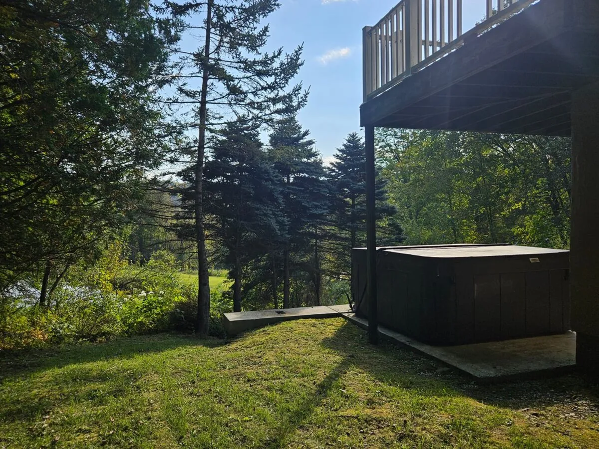This exterior shot shows a spacious deck with a hot tub nestled among trees. The views of nature from the deck provide a sense of seclusion and immersion in the mountain landscape, ideal for both relaxation and social gatherings. The image evokes the idea of enjoying starlit evenings or early mornings surrounded by natural beauty.